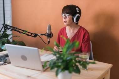 Middle-aged female radio presenter talking into the microphone and reading news - radio broadcast online concept
