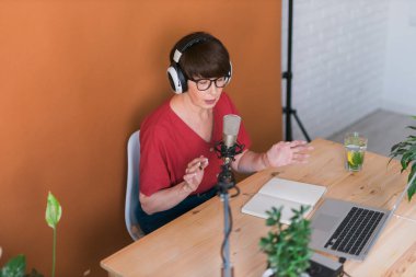 Middle-aged female radio presenter talking into the microphone and reading news - radio broadcast online concept
