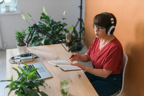 Middle-aged female radio presenter talking into the microphone and reading news - radio broadcast online concept