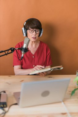 Middle-aged female radio presenter talking into the microphone and reading news - radio broadcast online concept