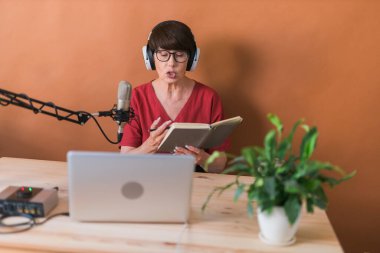 Mature woman making podcast recording for her online show. Attractive business woman using headphones front of microphone for a radio broadcast