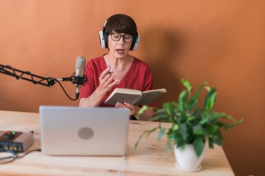 Middle-aged female radio presenter talking into the microphone and reading news - radio broadcast online concept