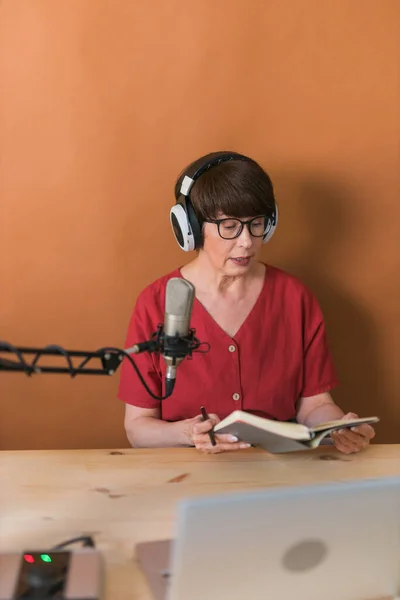 Middle-aged female radio presenter talking into the microphone and reading news - radio broadcast online concept — Stock fotografie