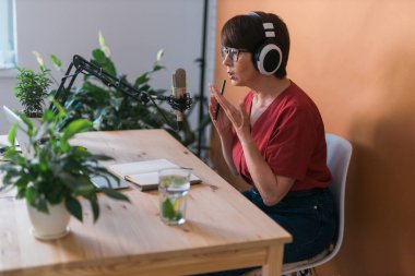 Portrait of mature woman wearing headphones and talking at online radio station - podcast and broadcast concept