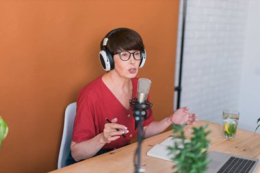 Middle-aged female radio presenter talking into the microphone and reading news - radio broadcast online concept