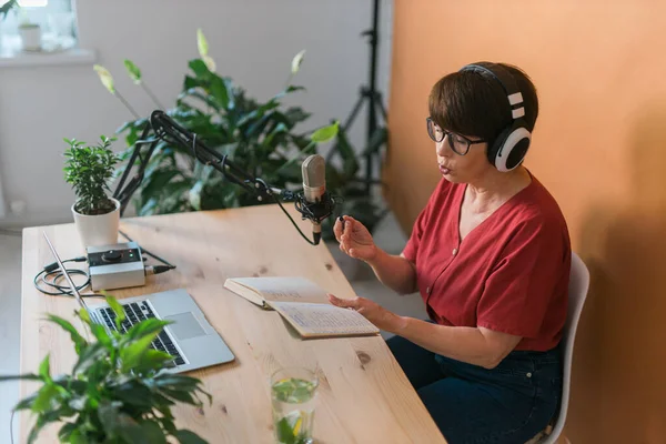 Middle-aged female radio presenter talking into the microphone and reading news - radio broadcast online concept