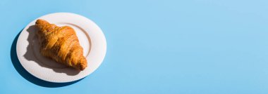 Fırın ürünleri beyaz tabakta pişmiş kruvasan. Mavi arka plan, üst manzara. Pop sanat tarzı. Yaz gölgeleri. Lezzetli ve yemek konsepti.