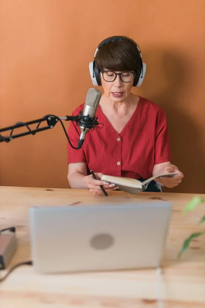 Middle-aged female radio presenter talking into the microphone and reading news - radio broadcast online concept — Stockfoto