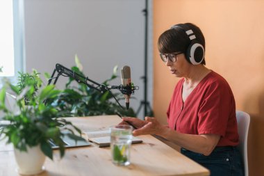 Middle-aged female radio presenter talking into the microphone and reading news - radio broadcast online concept