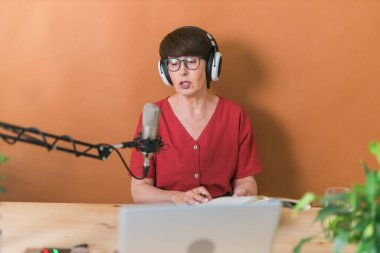 Portrait of mature woman wearing headphones and talking at online radio station - podcast and broadcast concept
