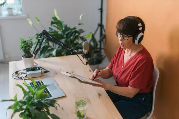 Middle-aged female radio presenter talking into the microphone and reading news - radio broadcast online concept
