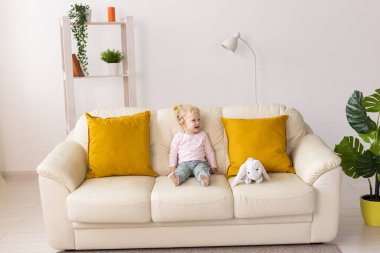Little girl with cochlear implant sitting on sofa at home. Hear impairment and deaf community concept
