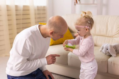 Baby child with hearing aids and cochlear implants plays with father on floor. Deaf and rehabilitation concept