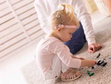 Cochlear implant for baby. Deaf child with hearing aid plays in living room.