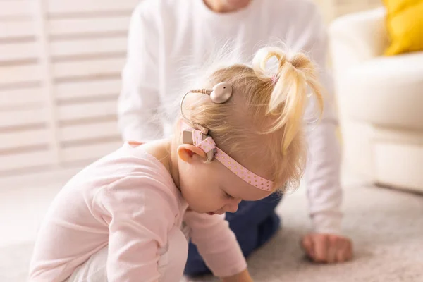 Cochlear implant for baby. Deaf child with hearing aid plays in living room. — Stock Fotó