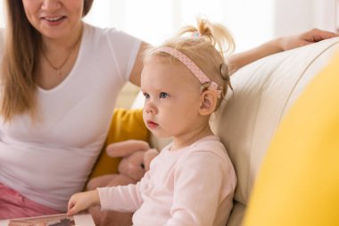 Child girl with cochlear implant with her mother at home. Hear impairment and deaf community concept
