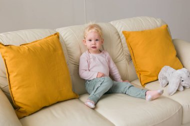 Kid with cochlear implants sits on sofa at home. Deafness and medical technology for hearing impaired patient concept.