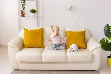 Kid with cochlear implants sits on sofa at home. Deafness and medical technology concept.