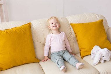 Kid with cochlear implants sits on sofa at home. Deafness and medical technology concept.