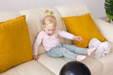 Kid with cochlear implants sits on sofa at home. Deafness and medical technology concept.