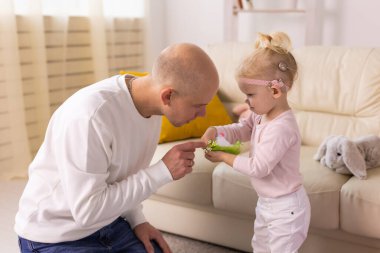 Baby with cochlear implants playing with her father at home. Deafness and medical technology concept