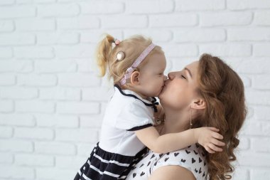 Anne, çocuğunu işitme cihazı ve koklear implantlarla beyaz tuğla duvarda tutuyor. Sağır ve sağlık kavramı