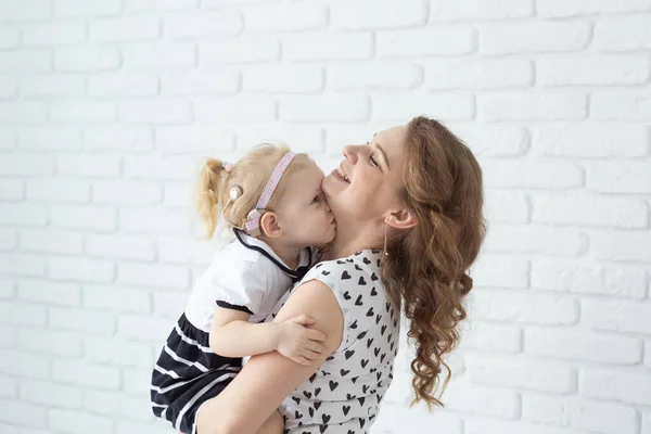 Mother holds her child with hearing aids and cochlear implants on white brick wall with copy space and place for advertising . Deaf and health concept