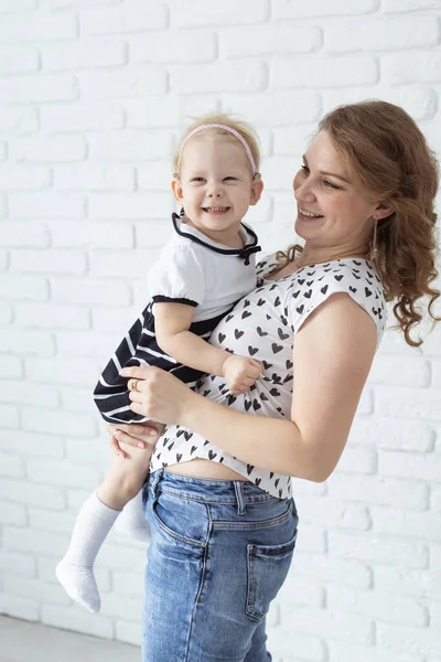 Anne, çocuğunu işitme cihazı ve koklear implantlarla beyaz tuğla duvarda tutuyor. Sağır ve sağlık kavramı