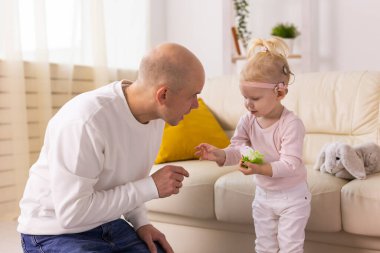 Baby girl with cochlear implants playing with her father at home. Deafness and medical technology concept