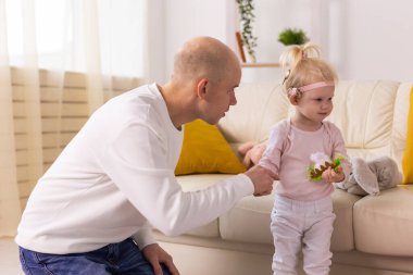 Baby girl with cochlear implants playing with her father at home. Deafness and medical technology concept