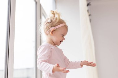 Funny baby with cochlear implant sitting at home and eating. Hear aid and medicine innovating technology and diversity concept