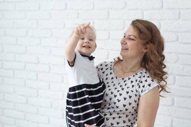 Mother holds and having fun her child with hearing aids and cochlear implants on white brick wall with copy space and place for advertising . Deaf and innovating medicine technologies concept