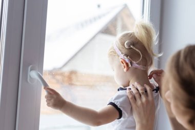 Mother fixing her daughters cochlear implant hearing aid - deafness and diversity concept. Innovative technologies in treatment of deafness