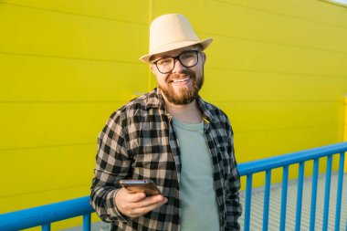 Bearded hipster guy in glasses using smartphone technology for making online booking and banking during travel vacations - millennial blogger with beard messaging social networks