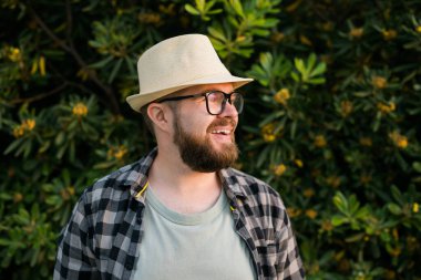 Laughing attractive man wearing hat over green tree background - emotion and vacation travel holidays