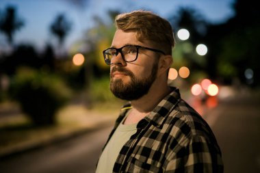 Portrait of man standing in night city street with bokeh street lights background. Confident lonely guy. Close-up portrait