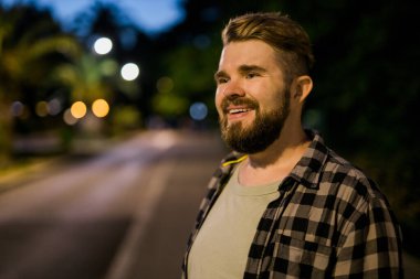 Portrait of man standing in night city street with bokeh street lights background. Confident lonely guy. Close-up portrait