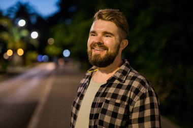 Portrait of man standing in night city street with bokeh street lights background. Confident lonely guy. Close-up portrait