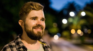 Portrait of man standing in night city street with bokeh street lights background. Confident lonely guy. Close-up portrait