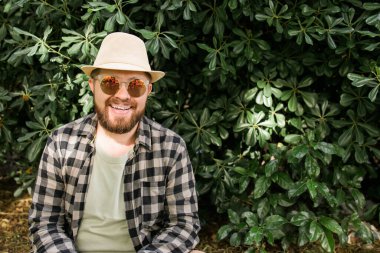 Laughing attractive man wearing hat over green tree background - emotion and vacation travel holidays