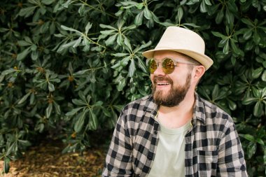 Laughing attractive man wearing hat over green tree background - emotion and vacation travel holidays
