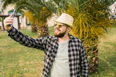 Man taking selfie portrait over palm tree background - Happy millennial guy enjoying summer holidays in city - Youth and technologies.