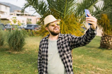 Man taking selfie portrait over palm tree background - Happy millennial guy enjoying summer holidays in city - Youth and technologies.