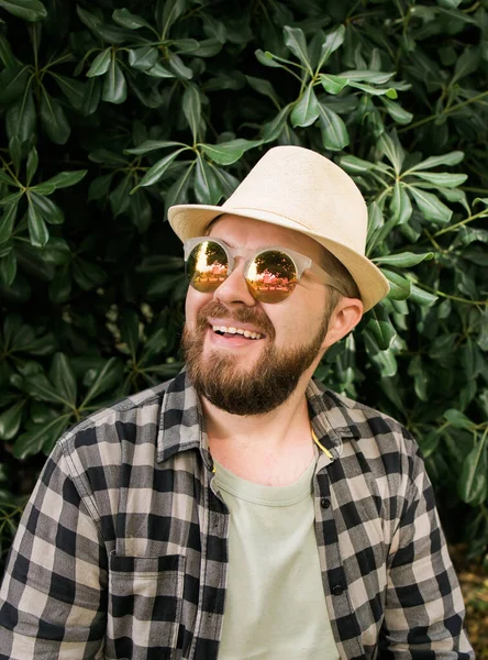 Laughing attractive man wearing hat over green tree background - emotion and vacation travel holidays