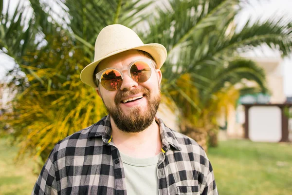 Laughing attractive man wearing hat over palm tree background - emotion and vacation travel holidays