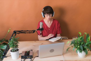 Middle-aged female radio presenter talking into the microphone and reading news - radio broadcast online