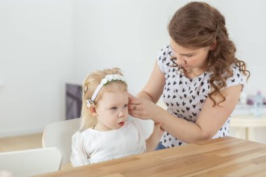 Anne, sağır kızının kulaklığına işitme cihazı takmasına yardım ediyor. Koklear implant ve yenilikçi tıp teknolojileri.