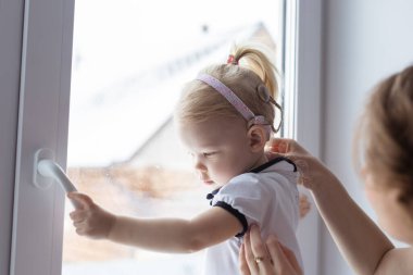 Anne, sağır kızının kulaklığına işitme cihazı takmasına yardım ediyor. Koklear implant ve yenilikçi tıp teknolojileri.