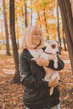 Sonbahar parkında köpeğini kucaklayan kıdemli bir kadın. Etkin yaşlanma ve evcil hayvan konsepti