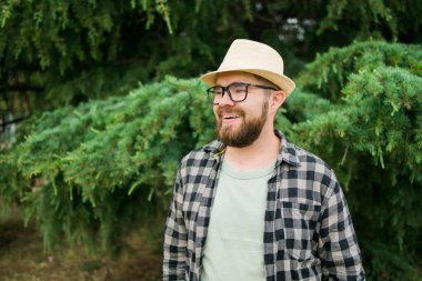 Laughing attractive man wearing hat over green tree background - emotion and vacation travel holidays